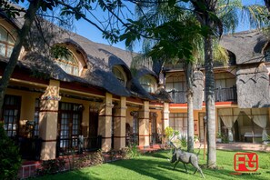 A traditional building with a thatched roof, multiple balconies, and a well-maintained garden with a statue. - Lalani Hotel and Conference Centre (Bulawayo)