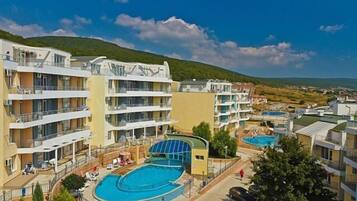 Un resort con varias construcciones, una piscina y montañas al fondo.