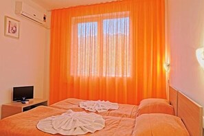 A hotel room with two beds, a TV on a side table, and an air conditioning unit on the wall.