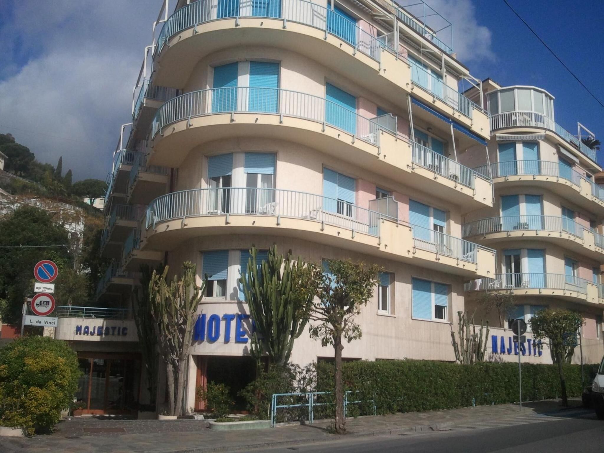 Un hotel a più piani con balconi, un cartello con la scritta 'Majestic Hotel' e un segnale di divieto di parcheggio.