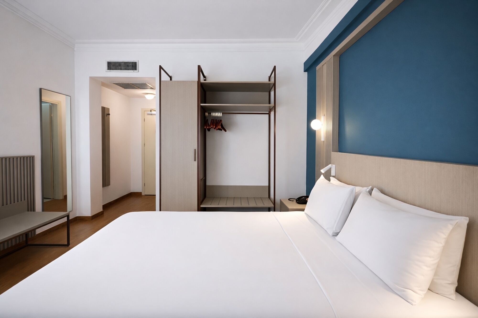 Une chambre d’hôtel comprenant un lit, une armoire, un miroir et une table de chevet.