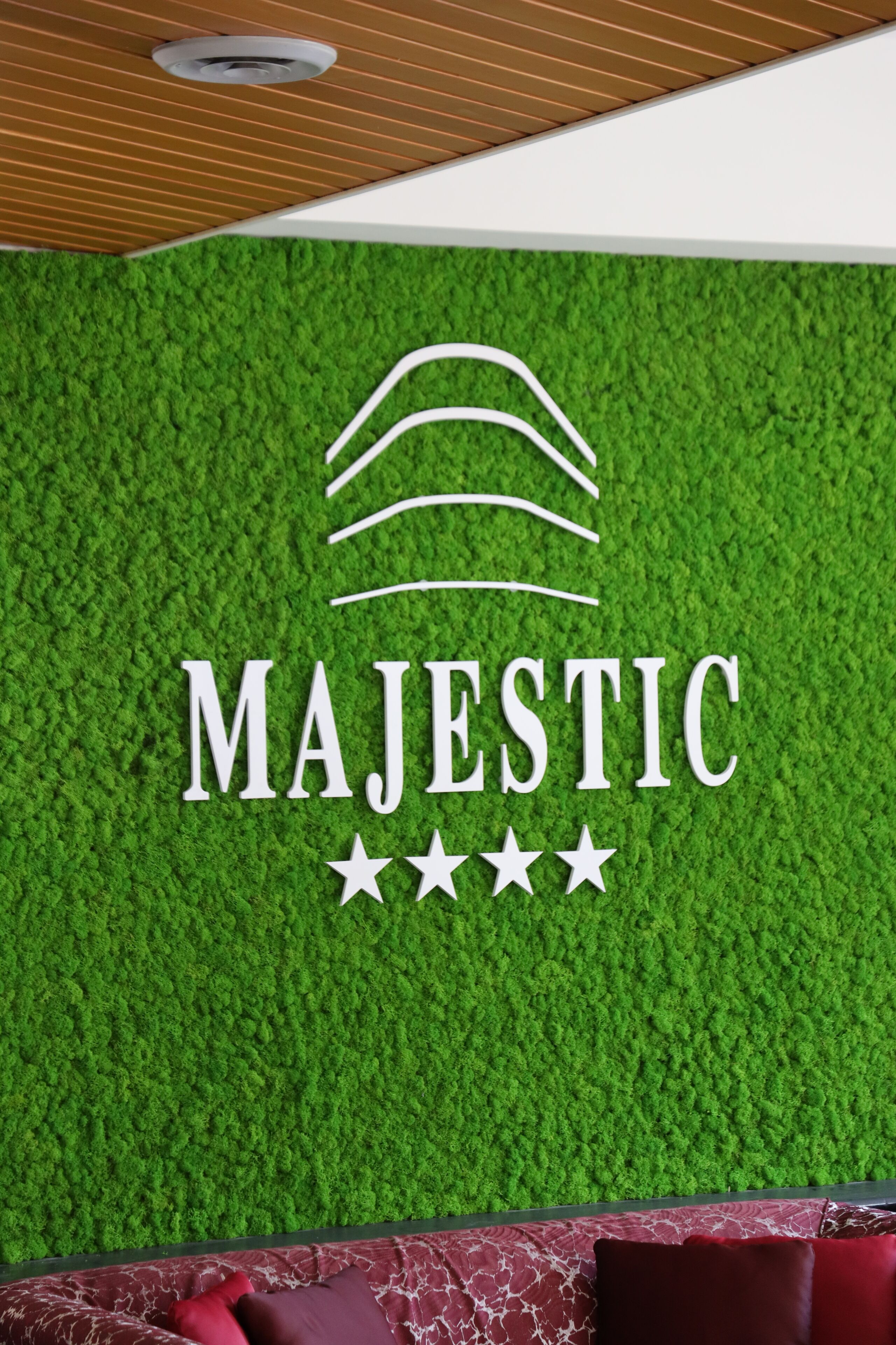 Een logo met het woord 'MAJESTIC' en drie sterren op een groen, reliëfbezet wand.