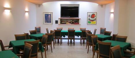 A dining area with round tables and chairs, a flat-screen TV mounted on the wall, and artwork on the walls.