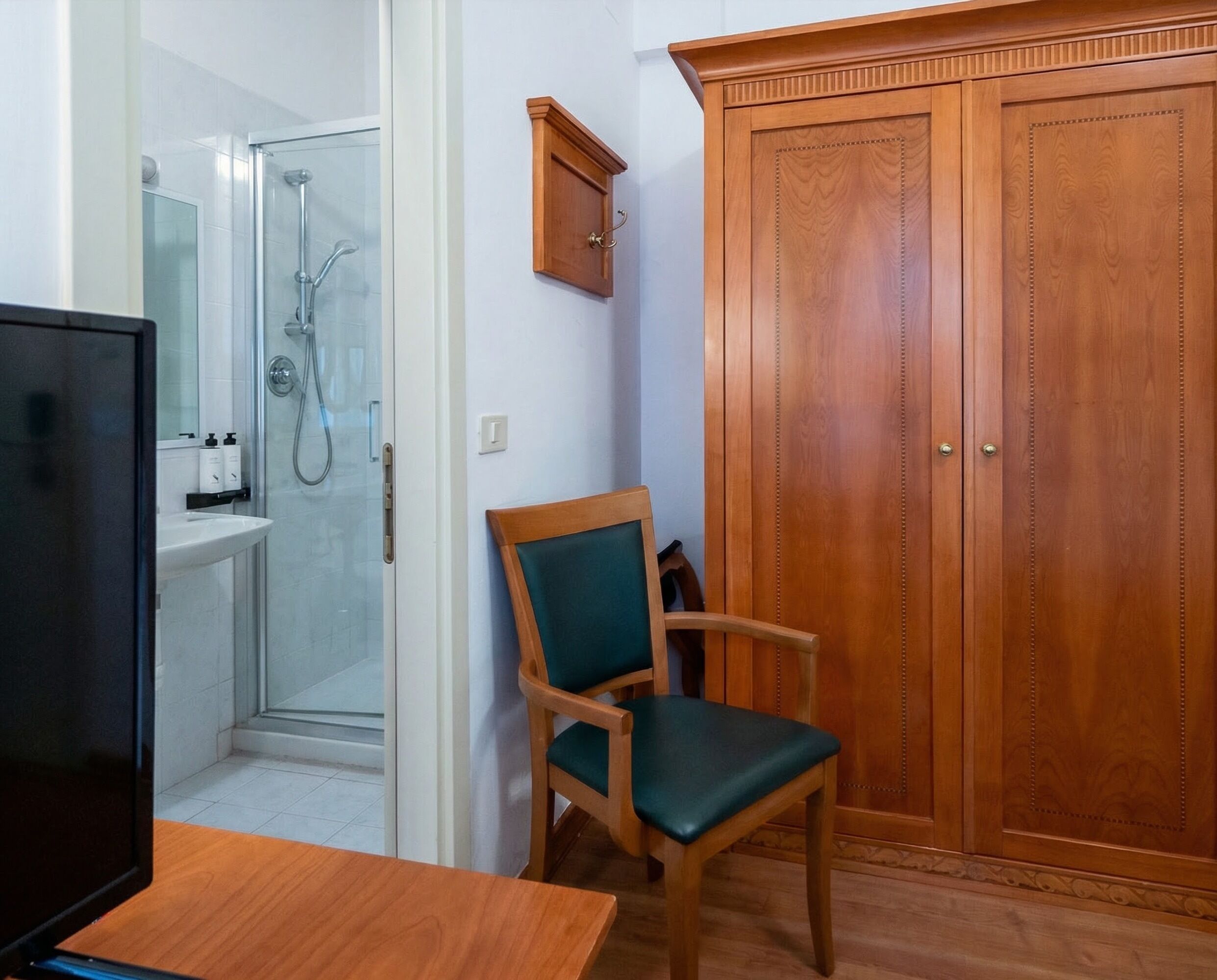 Une salle de bain avec une douche, une chaise en bois, une armoire en bois et un téléviseur posé sur une table en bois.