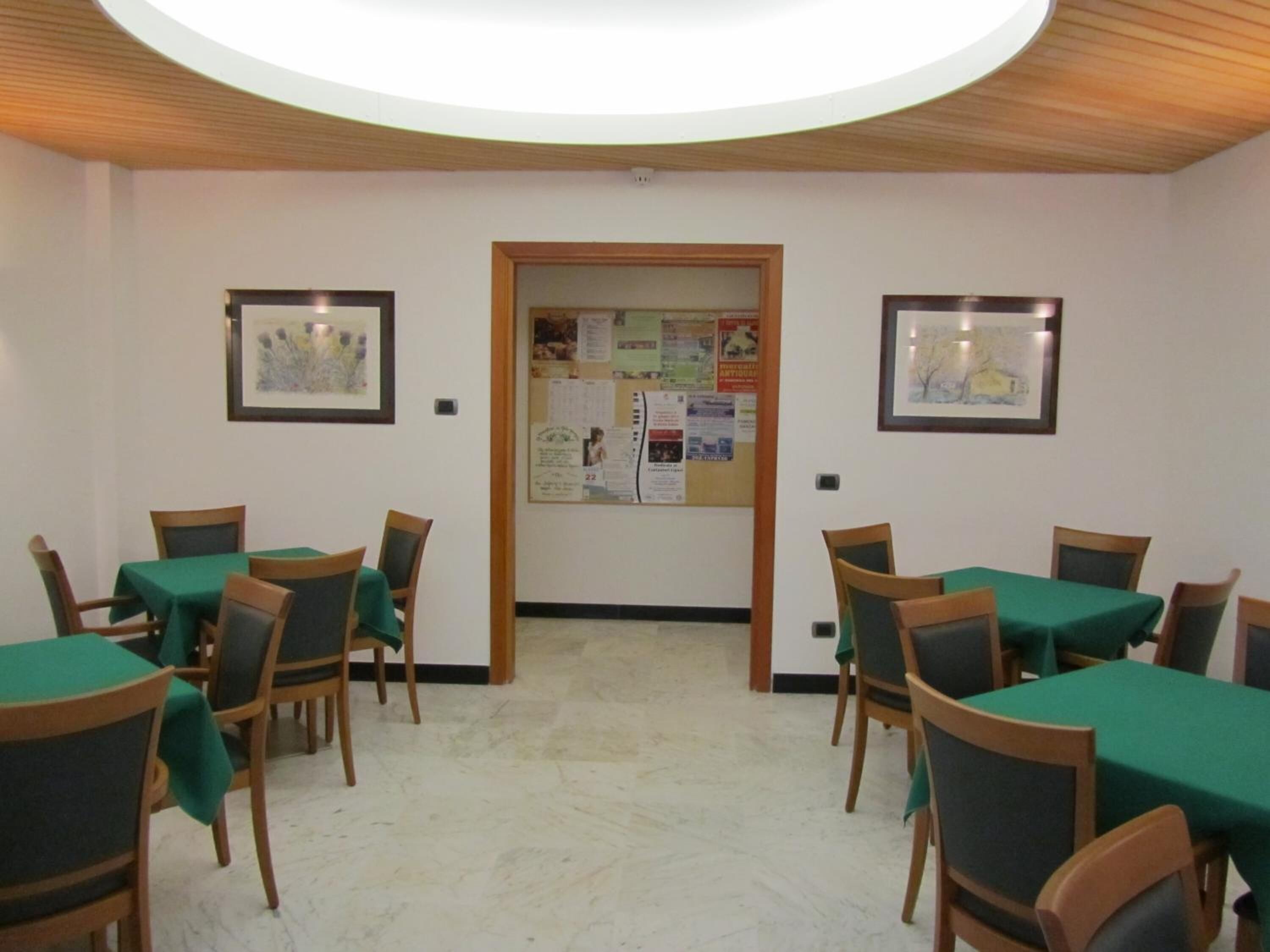 Uma área de refeições com mesas, cadeiras, um mural de avisos e quadros nas paredes.
