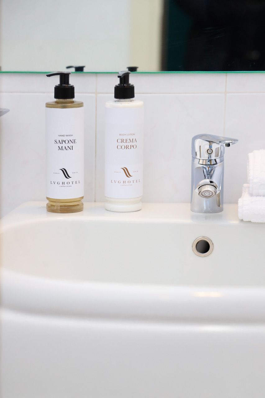 A bathroom with a white sink, two bottles of hand wash and body lotion, and a modern faucet.
