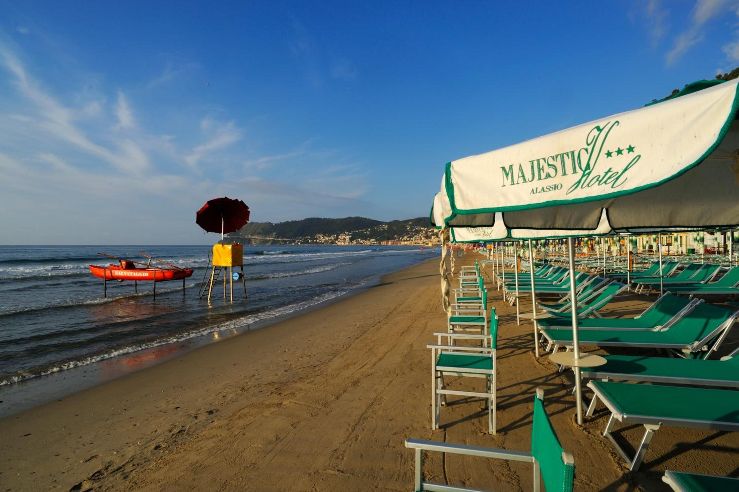 A beach with a row of green lounge chairs under a tent labeled "MAJESTIC Hotel".
