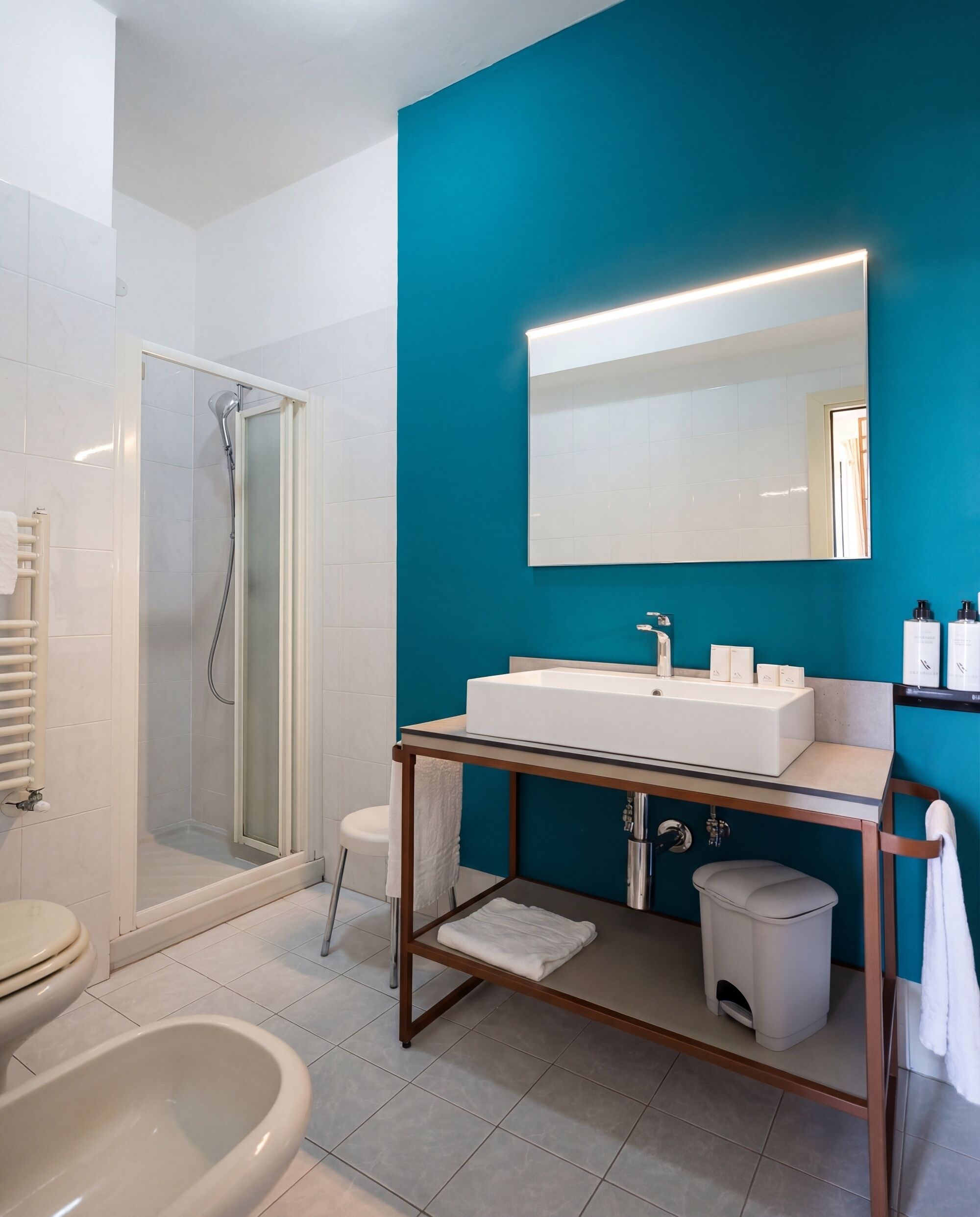 Un baño moderno con ducha envuelta en cristal, un lavamanos blanco con espejo superior y un inodoro blanco.