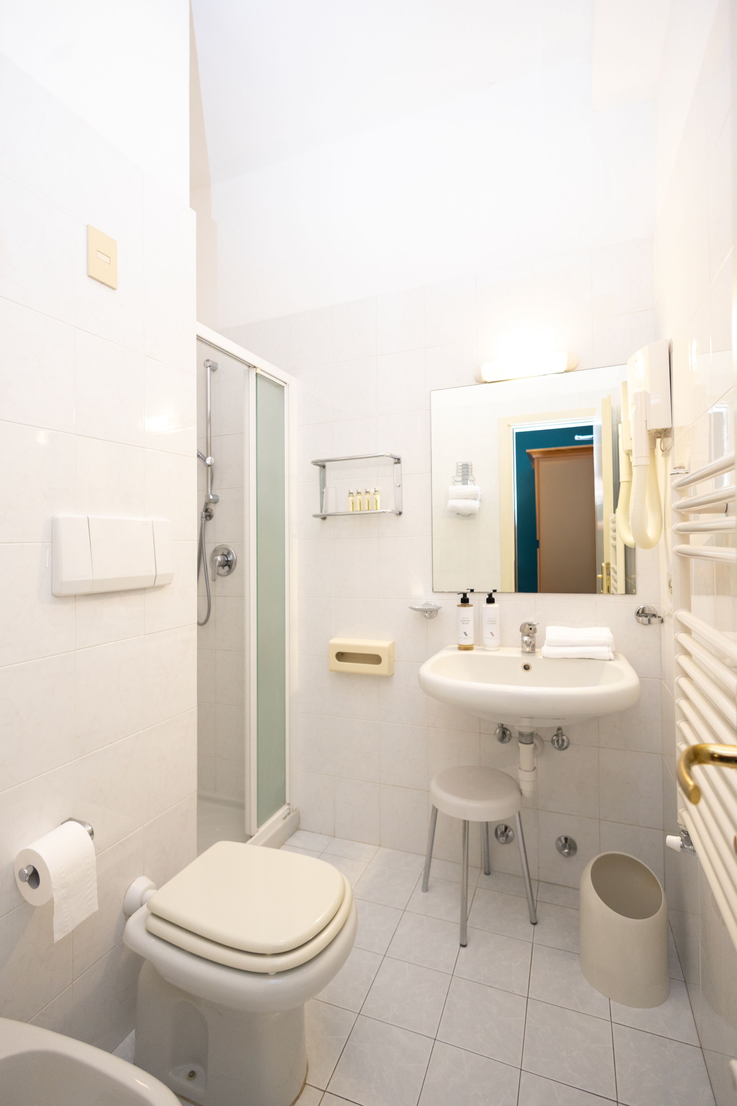 Ein Badezimmer mit Toilette, Waschbecken, Spiegel, Dusche und einem kleinen Hocker.