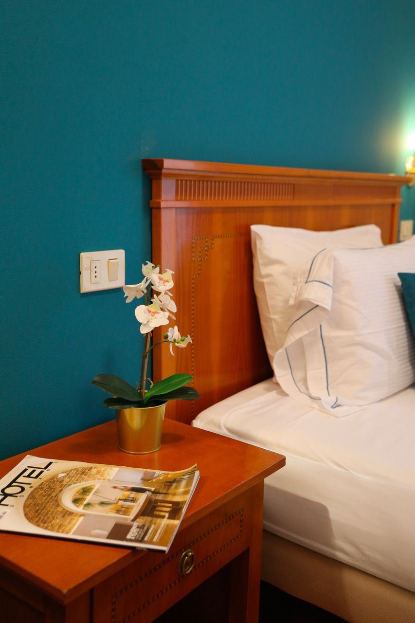 A hotel room with a wooden headboard, white bedding, a nightstand with a magazine, and a potted orchid.
