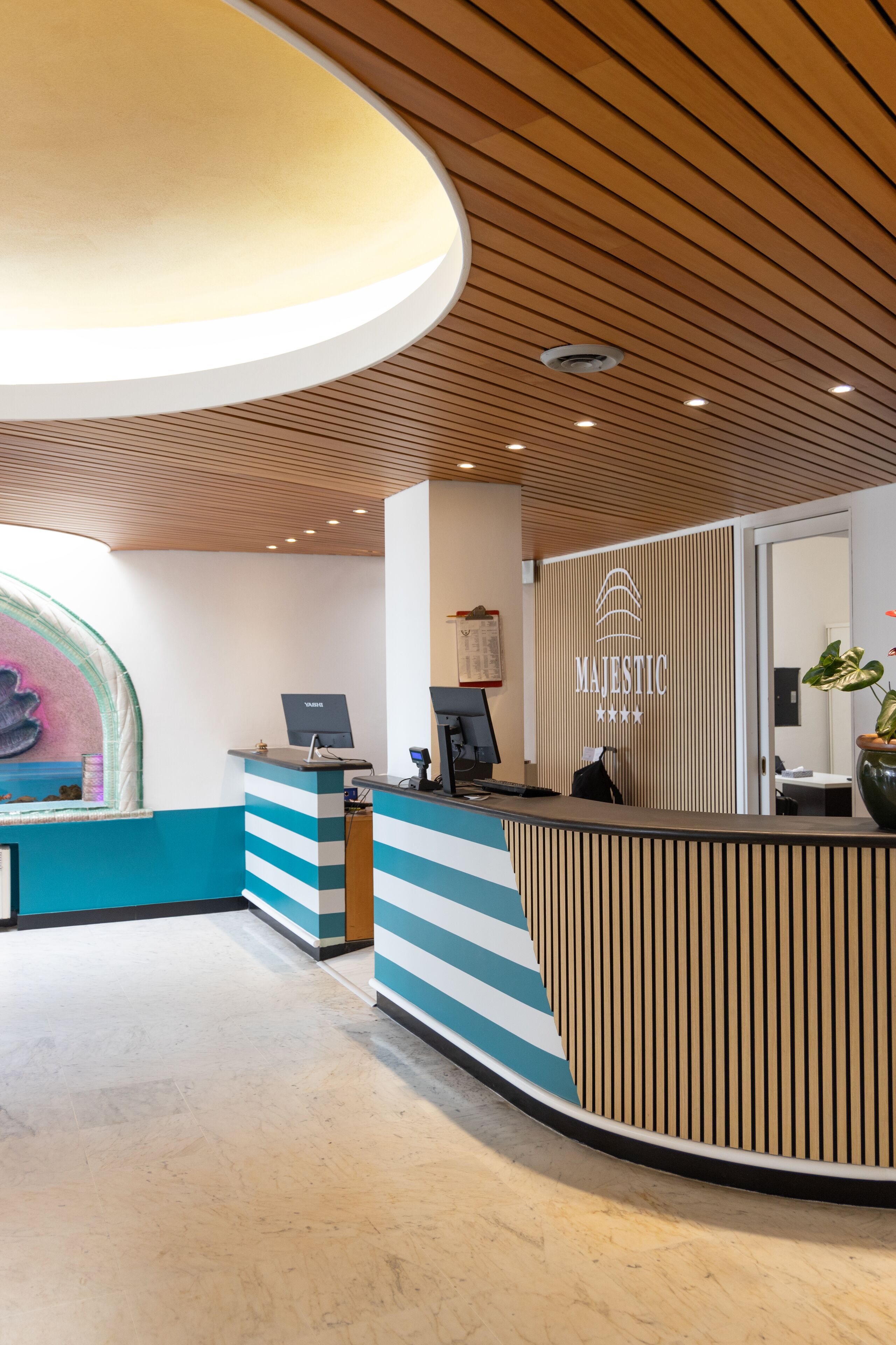 Ein Empfangsbereich mit modernem Design, der sich durch eine Holzdecke, eine Reception mit Streifenmuster und ein an der Wand befestigtes Schild mit der Aufschrift „MAJESTIC“ auszeichnet.