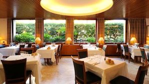 A restaurant with multiple tables, each set with cutlery and glasses, and large windows offering a view of greenery. - LVG Hotel Collection - Majestic (Alassio)