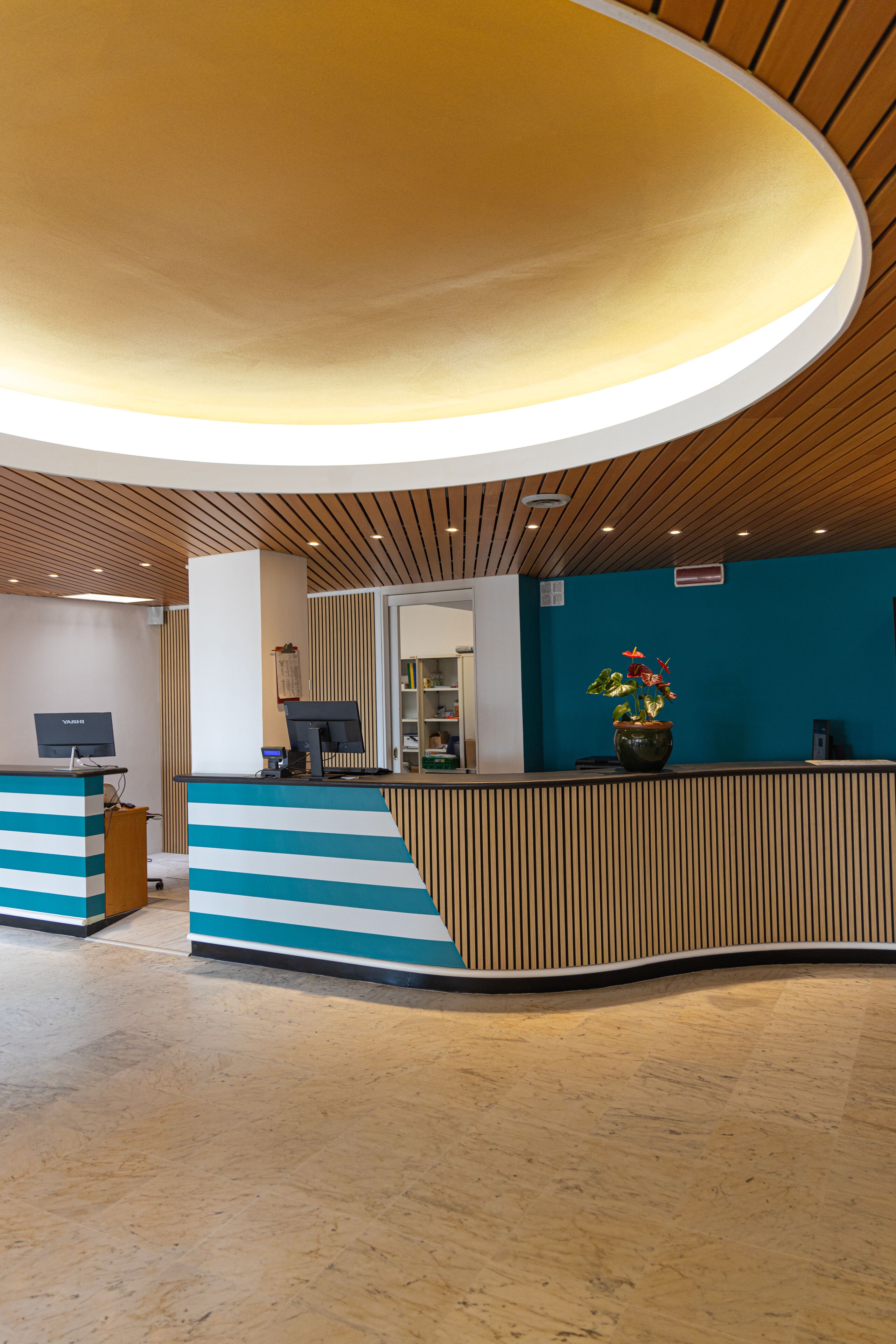 A reception area with a curved ceiling, a reception desk, a computer, and a potted plant.