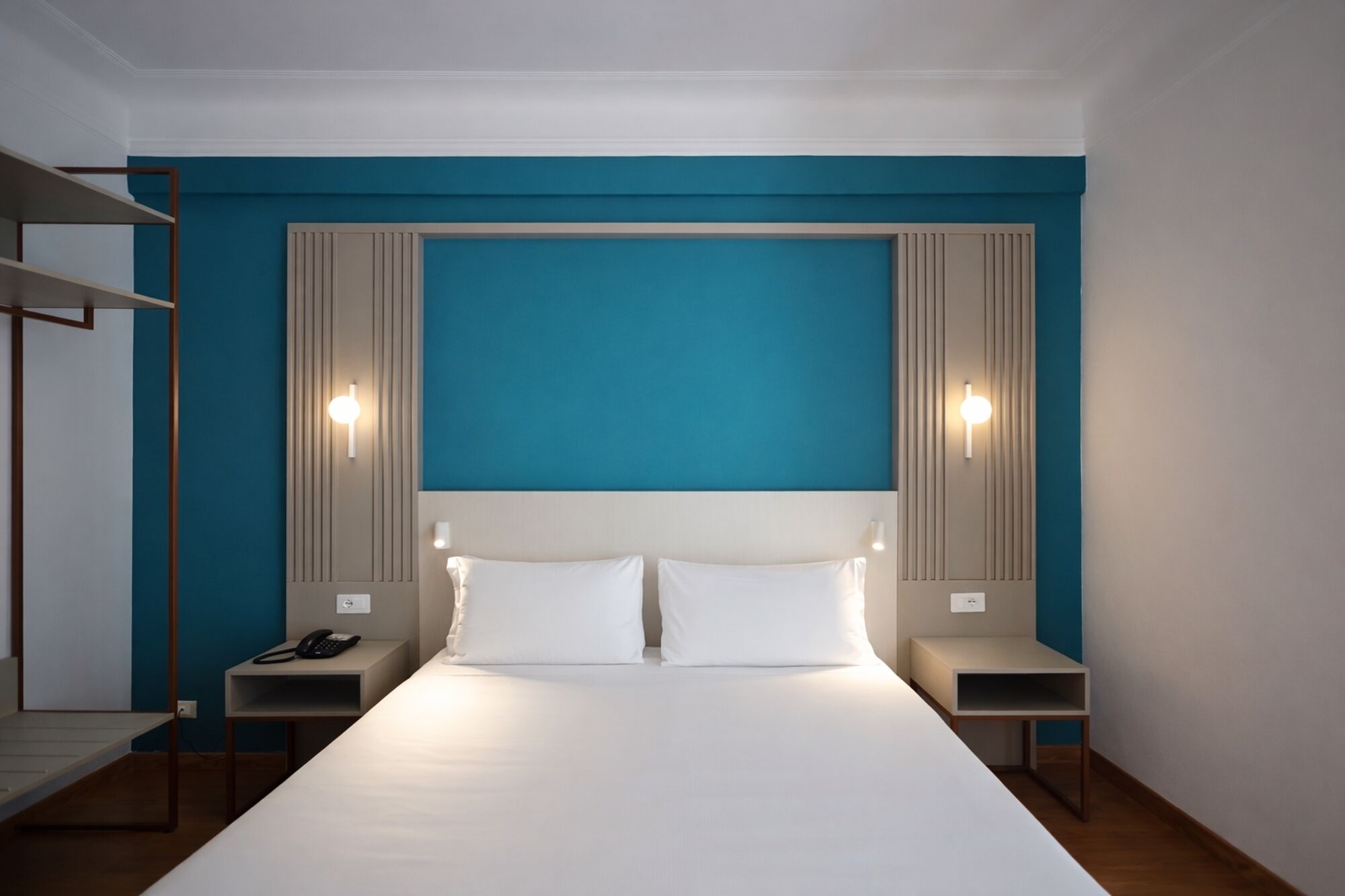 Une chambre d’hôtel avec un grand lit, deux tables de chevet, un téléphone et une étagère.