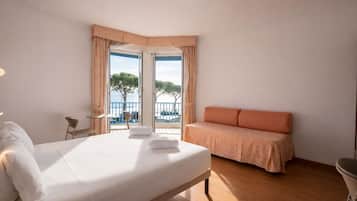 Una habitación de hotel con cama, zona de estar, vista al mar y balcón.