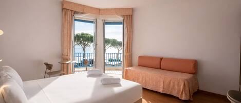 A hotel room with a bed, a seating area, a view of the sea, and a balcony.