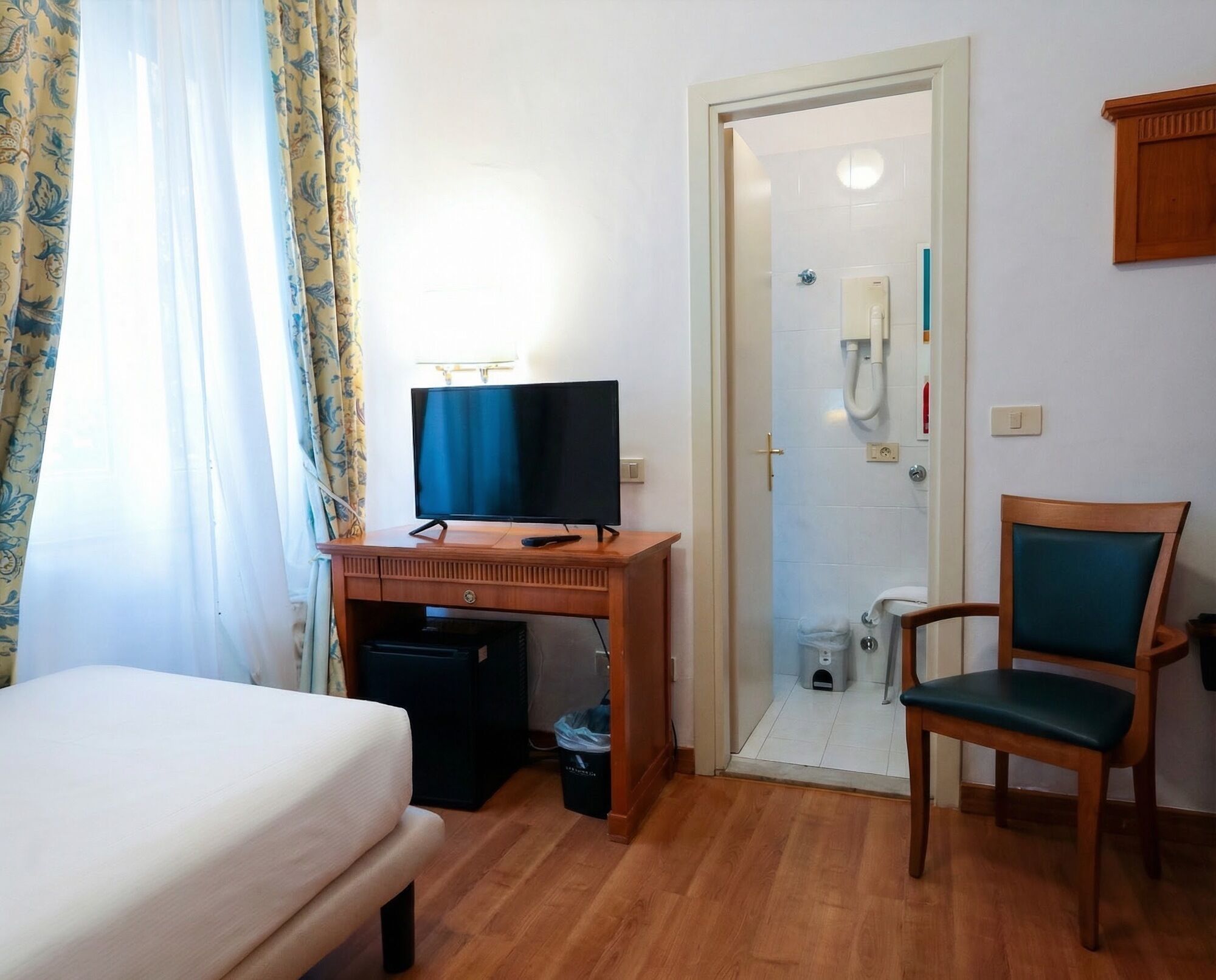 Hotellihuone, jossa on sänky, työpöytä, jossa on televisio, tuoli ja suihkutila.