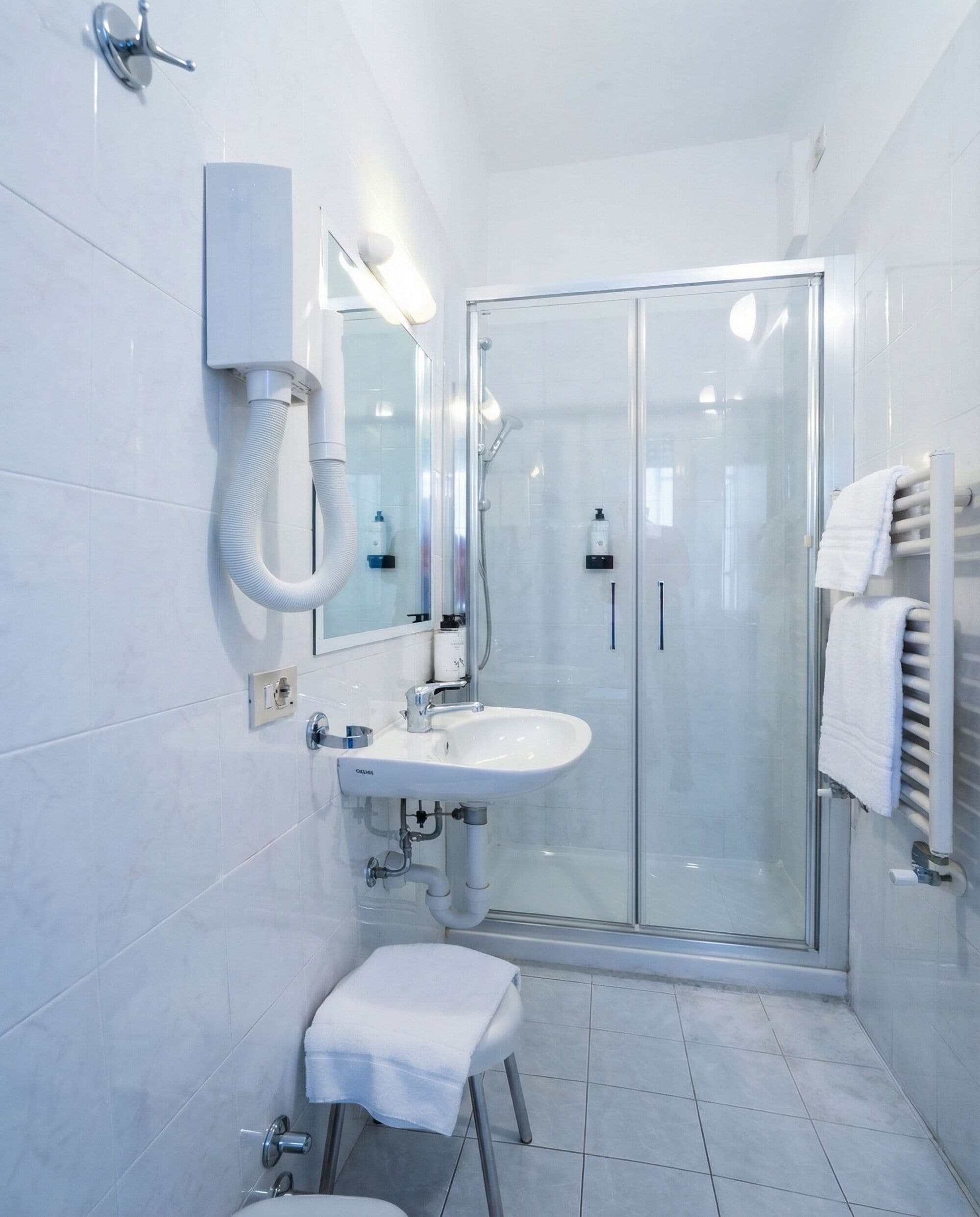 Een moderne badkamer met een glazen douchecabine, een witte wastafel en een klein krukje.