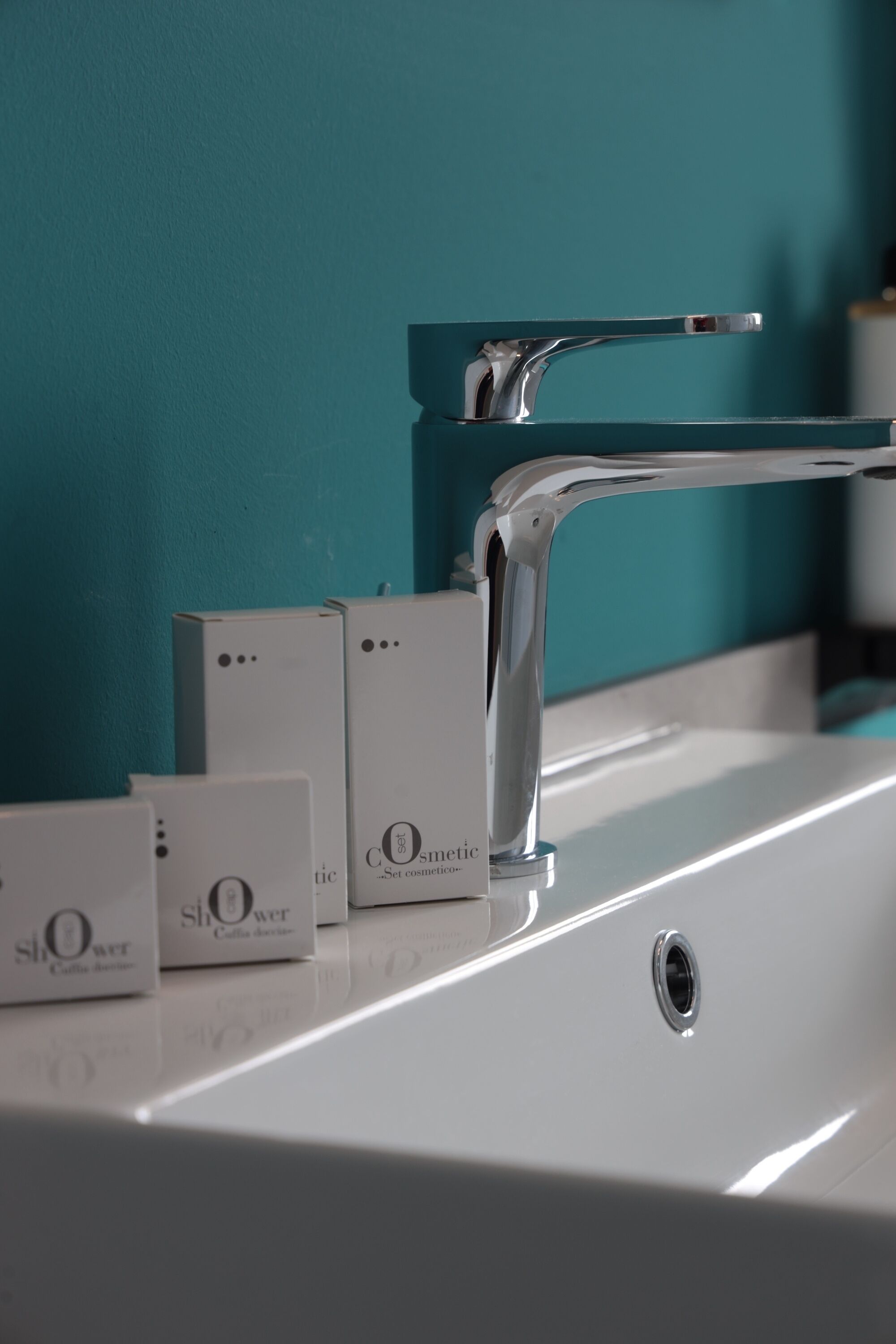 A bathroom with a chrome faucet, a white sink, and a teal wall.