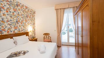 Habitación de hotel con cama, armario de madera, una silla y vistas a través de un ventanal.