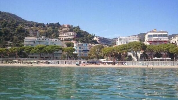 A coastal town with buildings on a hillside, a beach with umbrellas, and clear blue water. - LVG Hotel Collection - Majestic (Alassio)