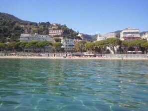 A coastal town with buildings on a hillside, a beach with umbrellas, and clear blue water. - LVG Hotel Collection - Majestic (Alassio)