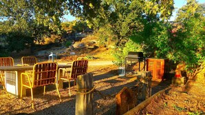An outdoor dining area with metal chairs and tables, a barbecue grill, and a wooden fence. - Quinta das Lavandas (Castelo de Vide)