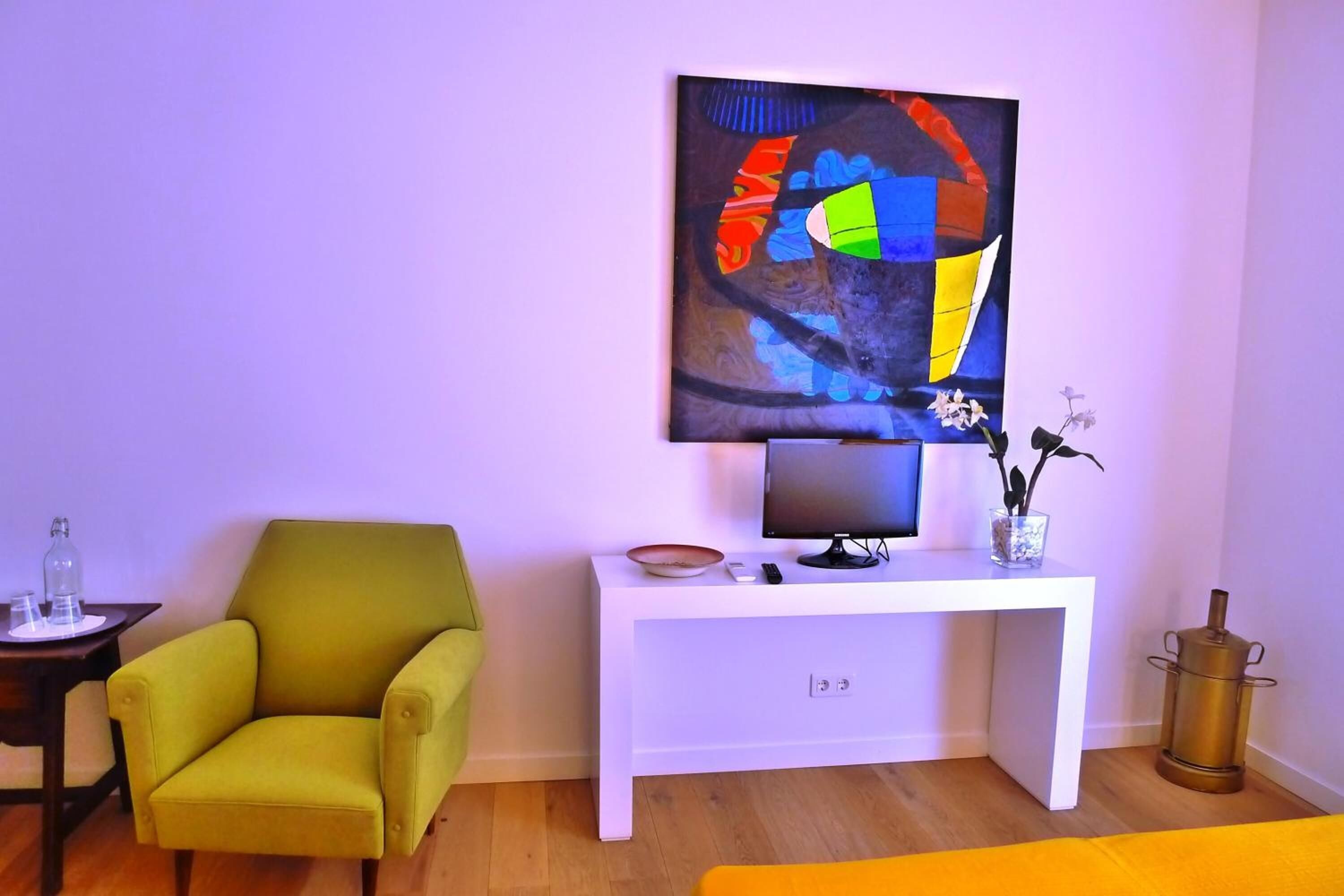A modern living room with a green armchair, a white console table with a flat-screen TV, a vase with flowers, and a decorative metal object.