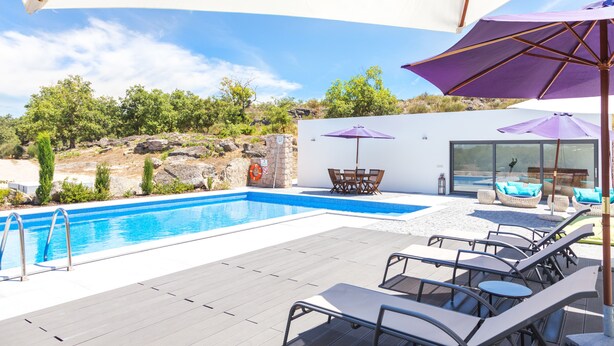 A swimming pool with lounge chairs and umbrellas, surrounded by a wooden deck and a stone wall. - Quinta das Lavandas (Castelo de Vide)