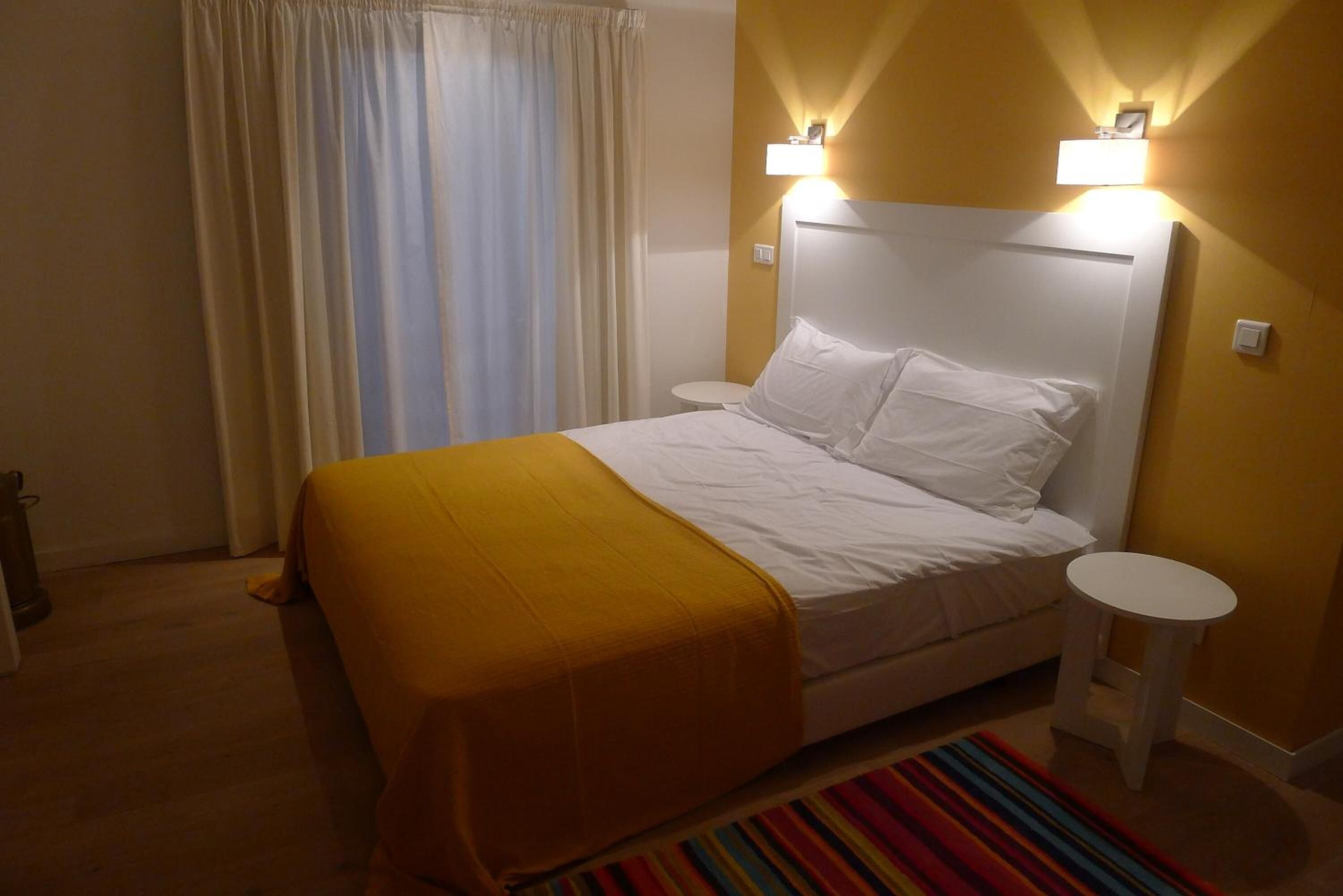 Hotellihuone, jossa on sänky, yöpöydät, pieni pyöreä pöytä ja värikäs raidallinen matto.