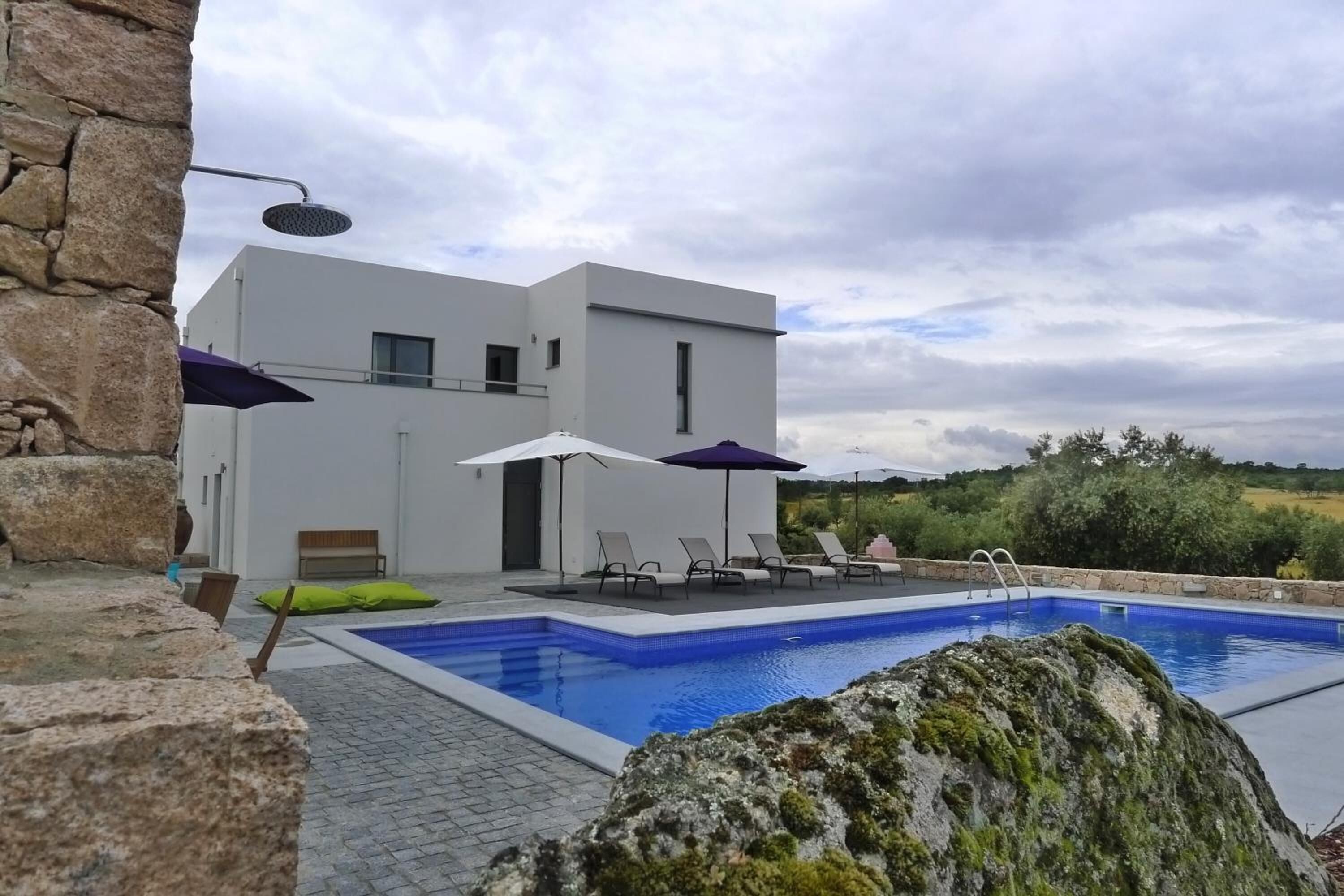 A modern pool area with a rectangular pool, lounge chairs, and umbrellas.