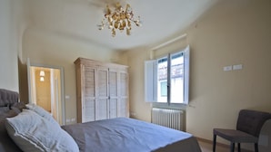 A bedroom with a bed, a chair, a wardrobe, and a window with blinds. - Alfani Luxury Loft (Florence)