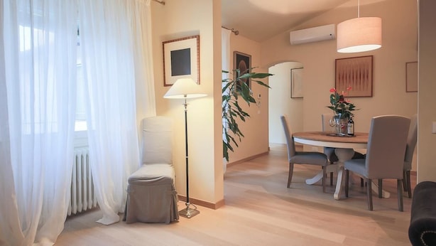 A modern living room with a dining area, featuring a sofa, a lamp, a dining table with chairs, and a large plant. - Alfani Luxury Loft (Florence)