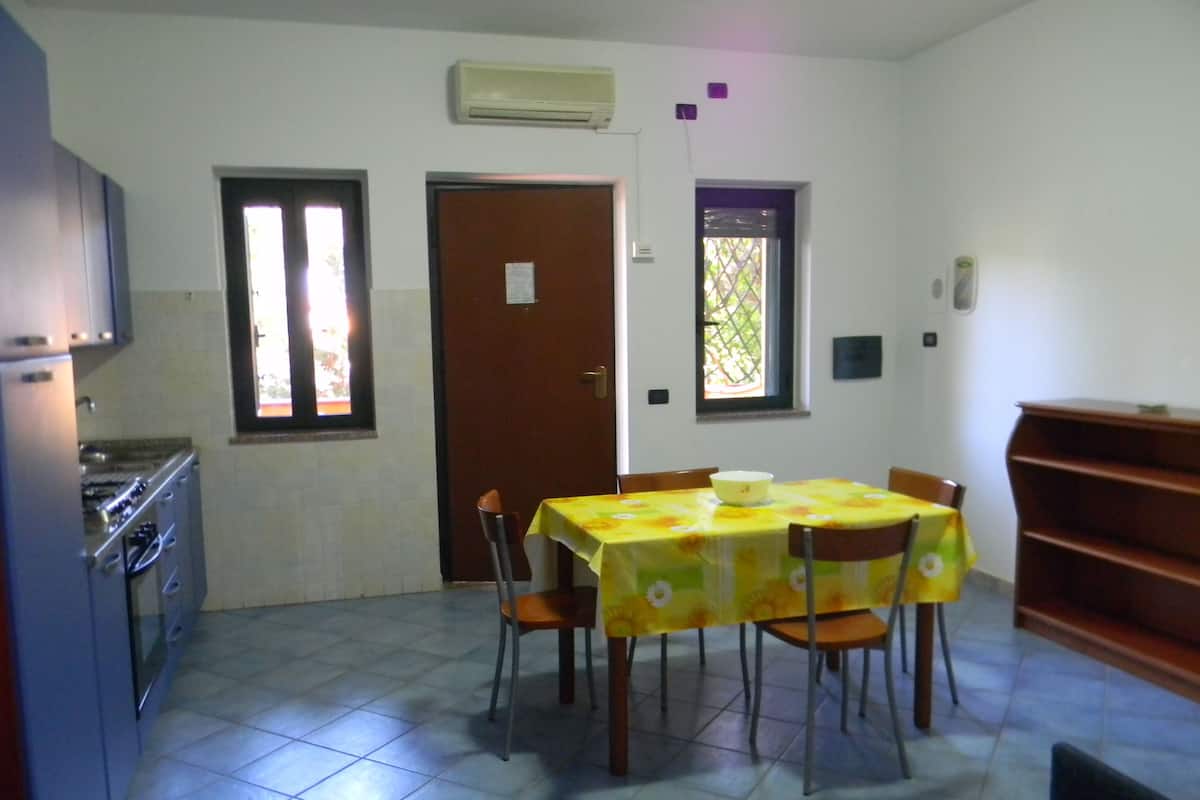 A dining area with a table set for four, a kitchen with a stove, and a door leading to another room.