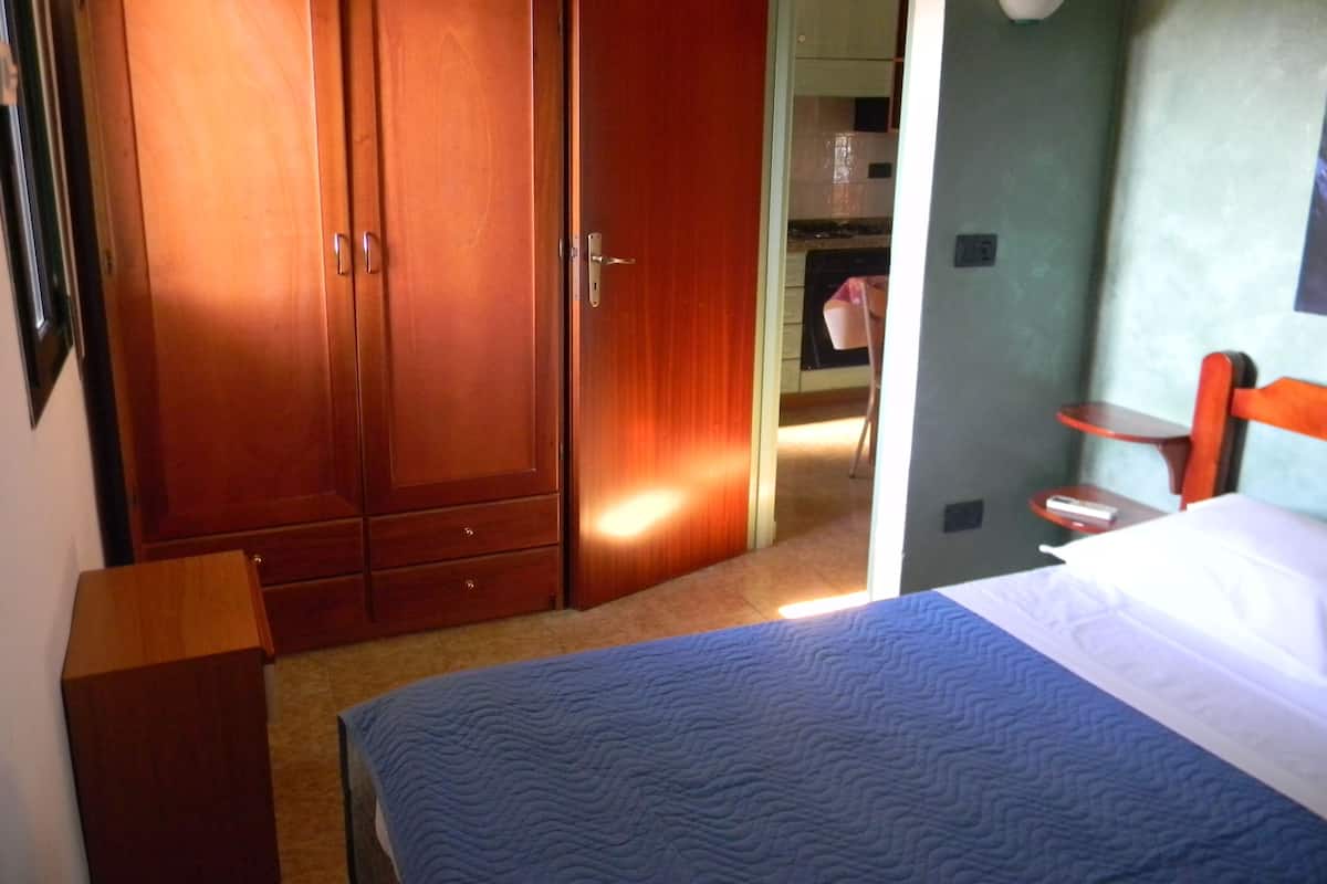 A bedroom with a bed, a wooden wardrobe, a small table, and a chair.