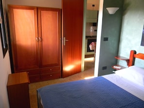 A bedroom with a bed, a wooden wardrobe, a small table, and a chair.