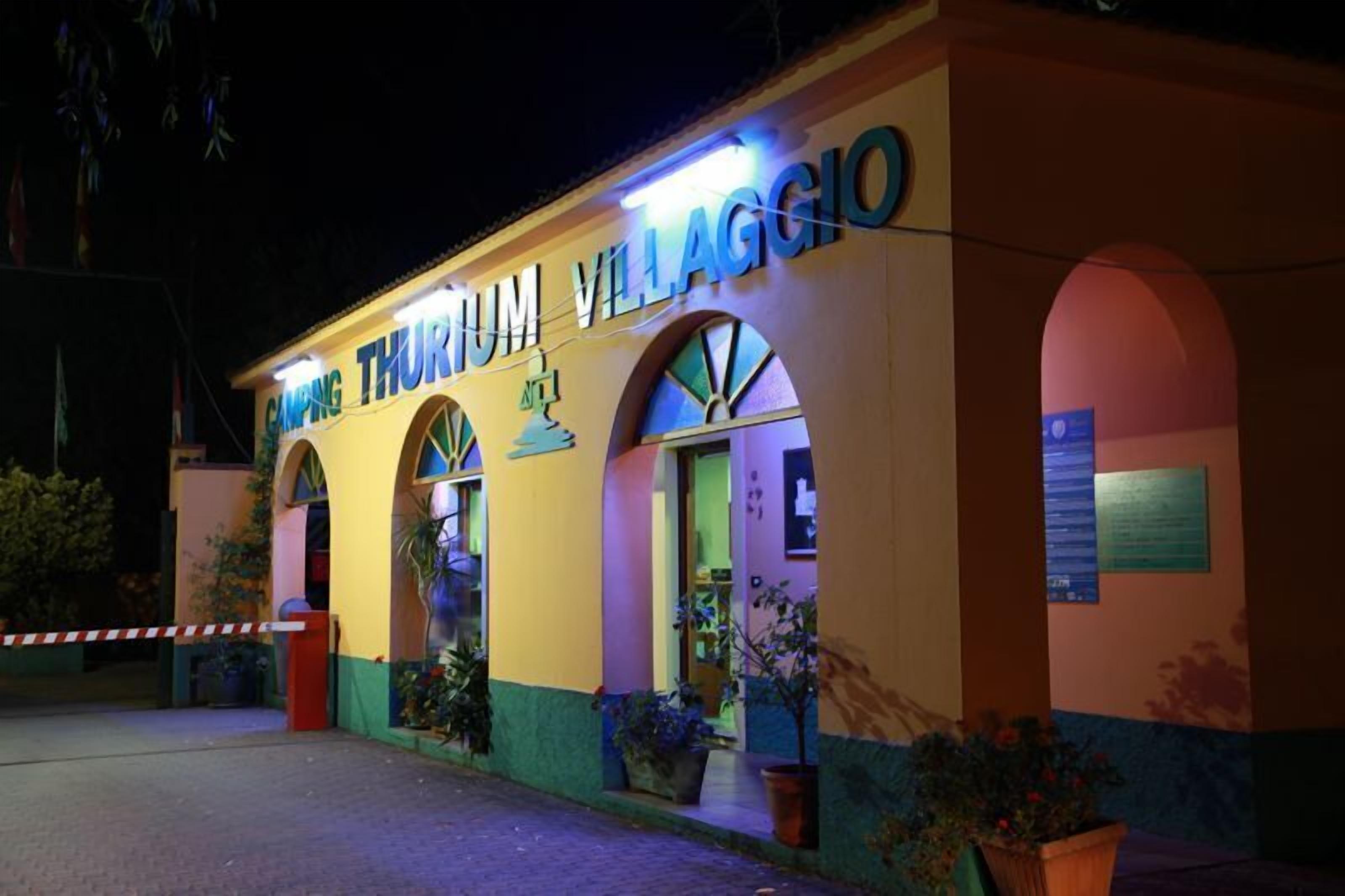 Ein Gebäude mit der leuchtenden Beschilderung „CAMPING THURIUM VILLAGGIO“ bei Nacht.