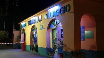 Ein Gebäude mit der leuchtenden Beschilderung „CAMPING THURIUM VILLAGGIO“ bei Nacht.