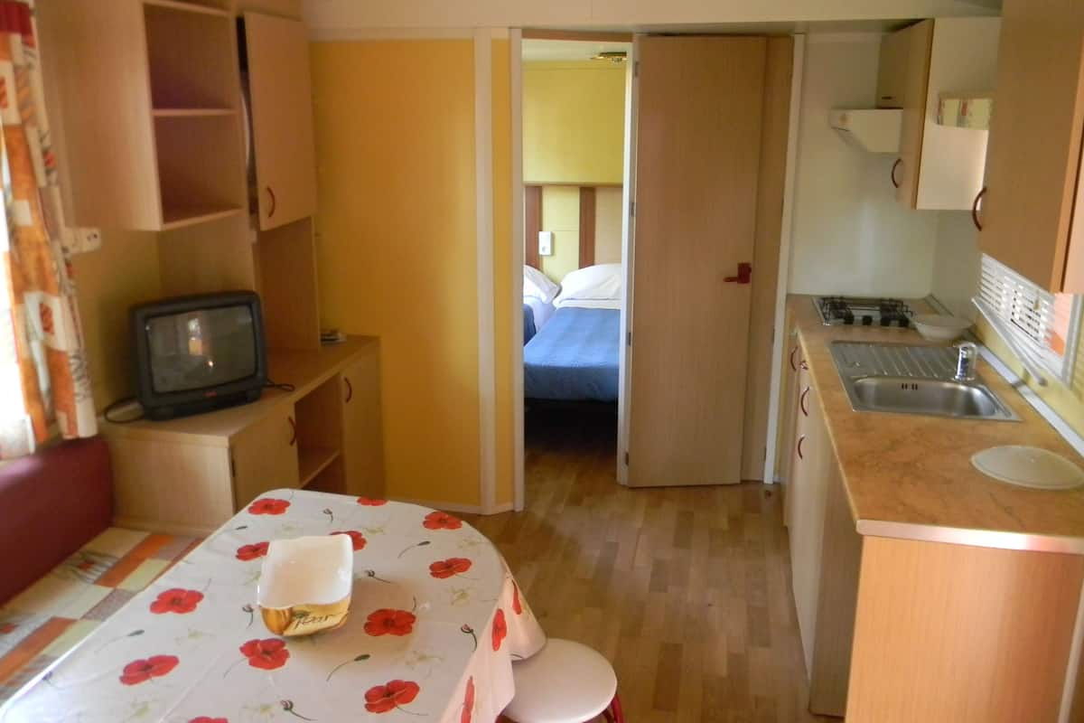 A compact room with a bed, a small kitchenette, a television, and a table with a floral tablecloth.