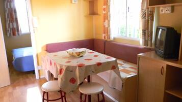 Un rincón comedor acogedor con una mesa cubierta por un mantel floral, dos taburetes, un banco acolchado y un televisor sobre un mueble de madera.