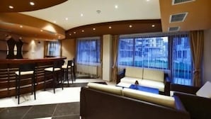A modern living room with a curved ceiling, a bar area with stools, and large windows with curtains. - Belmont (Bansko)