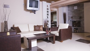 A modern lobby with a sofa, armchairs, a coffee table, a TV, and a fireplace. - Belmont (Bansko)