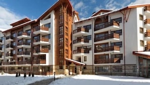A multi-story hotel with balconies and a ski slope in the background. - Belmont (Bansko)
