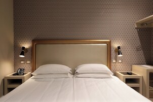 Hotellihuone, jossa on suuri sänky, kaksi yöpöytää, puhelin ja seinään kiinnitetyt lamput.