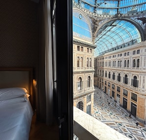 Une chambre d’hôtel dotée d’une grande fenêtre donnant sur la cour intérieure d’un bâtiment historique, dont le plafond est en verre.