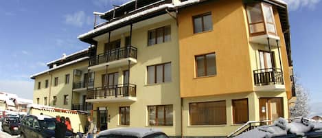 A multi-story building with balconies, parked cars, and snow on the roof.