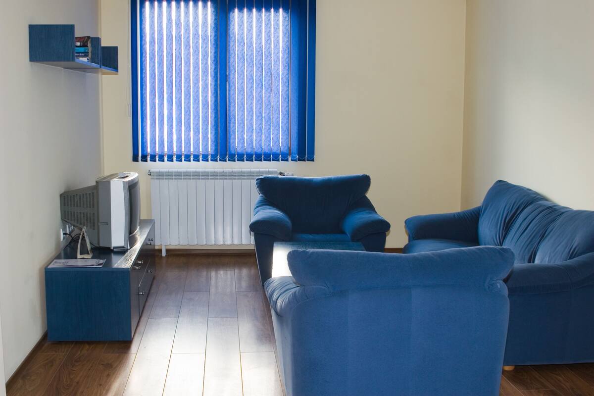 A living room with a blue sofa, a small table with a television, and a radiator.