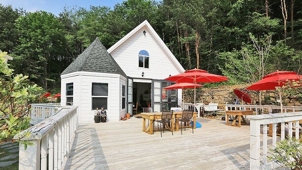 A white building with a grey roof, a wooden deck, and red umbrellas. - Kismet Cottage (Pyeongchang)
