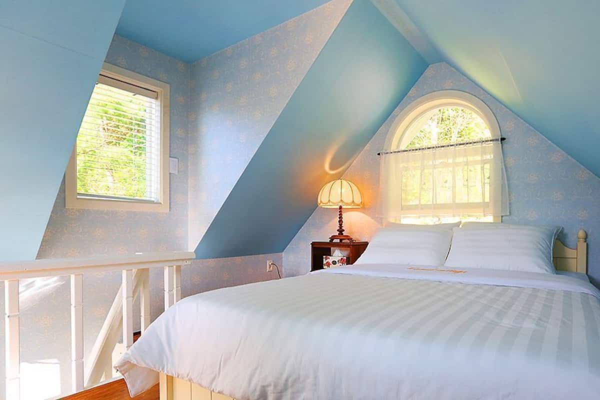 A bedroom with a bed, a nightstand, a lamp, a window, and a balcony.