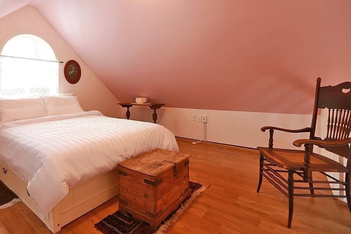 A bedroom with a bed, wooden chest, chair, and a small table with a lamp.